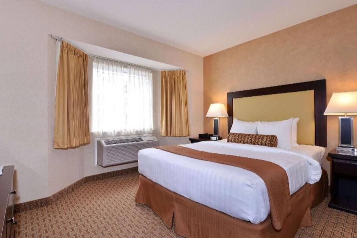 A hotel room with a large bed, two bedside lamps, a desk with a chair, and a window with curtains.