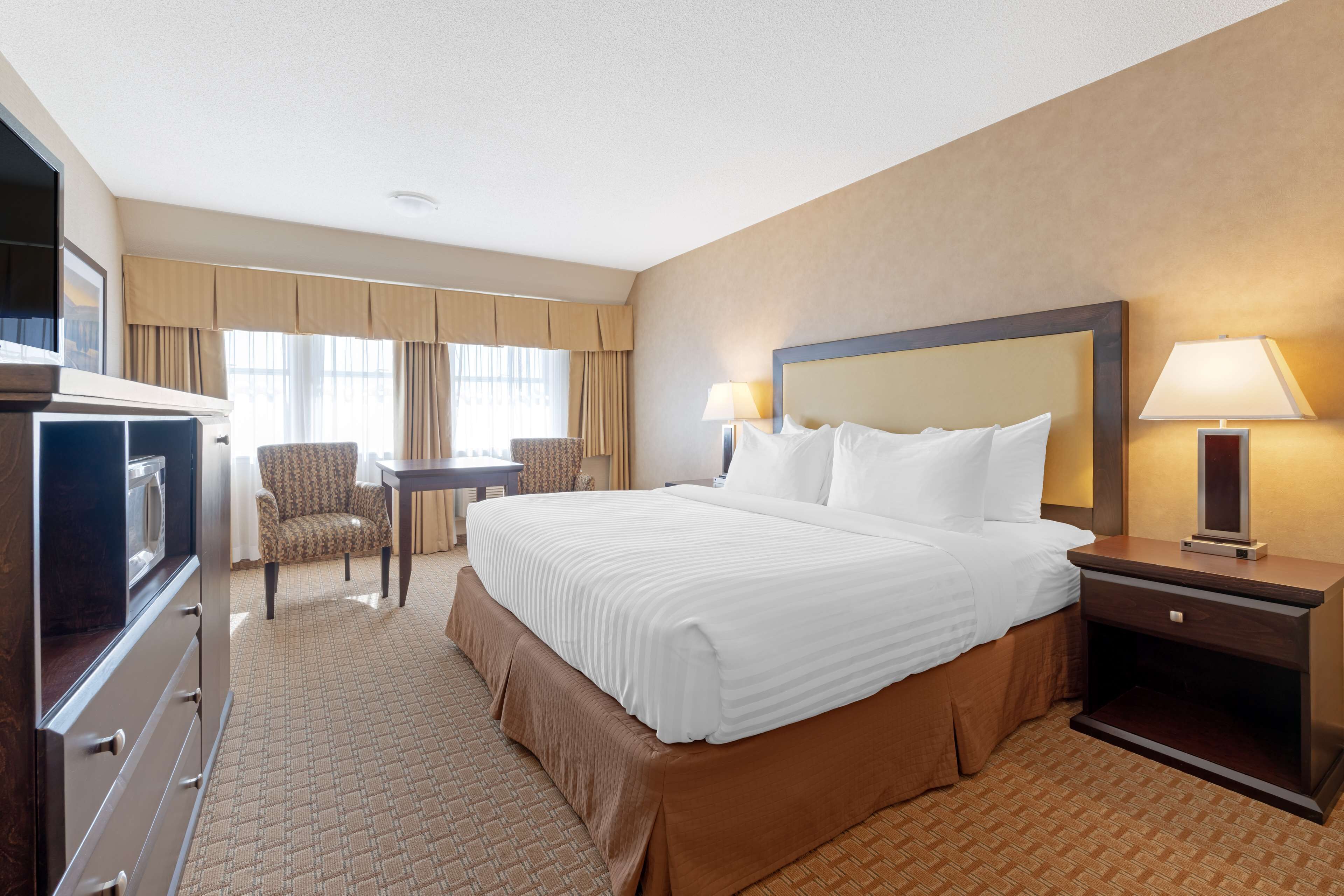 A hotel room with a large bed, a desk, a chair, and a TV.