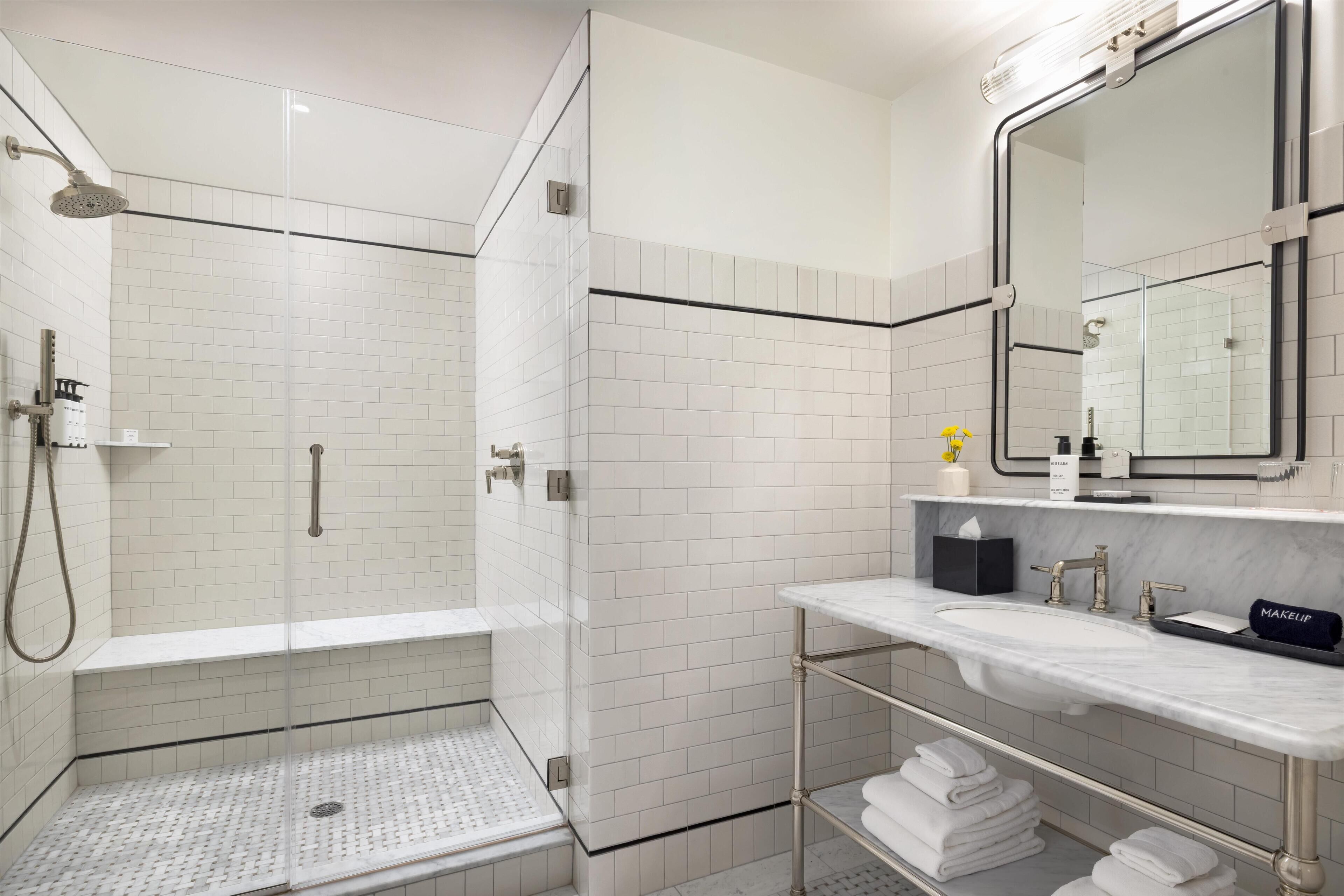 A modern bathroom with white subway tiles, a glass-enclosed shower, a marble sink, and a large mirror.