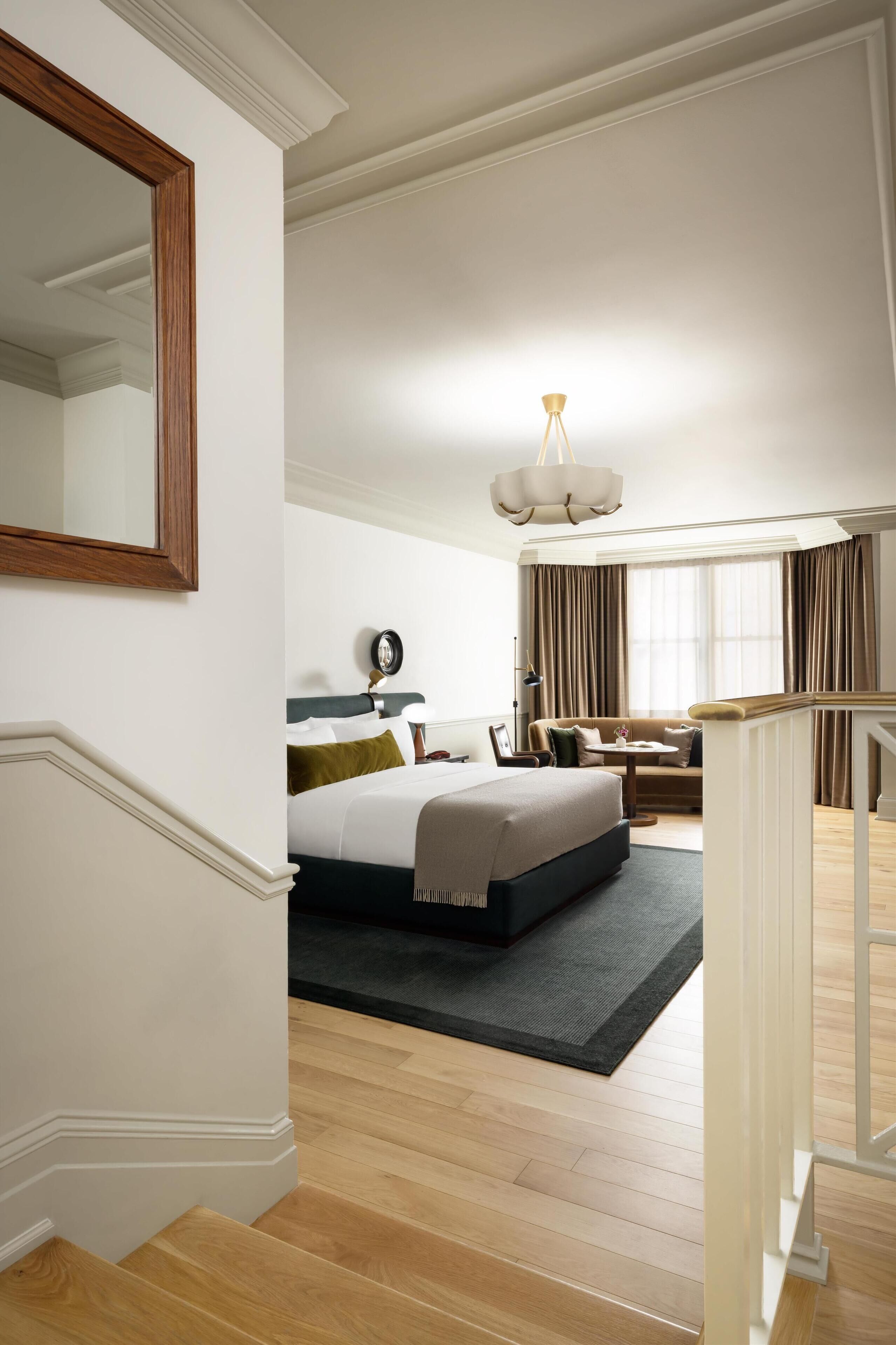 A spacious bedroom with a large bed, a seating area, and a staircase.