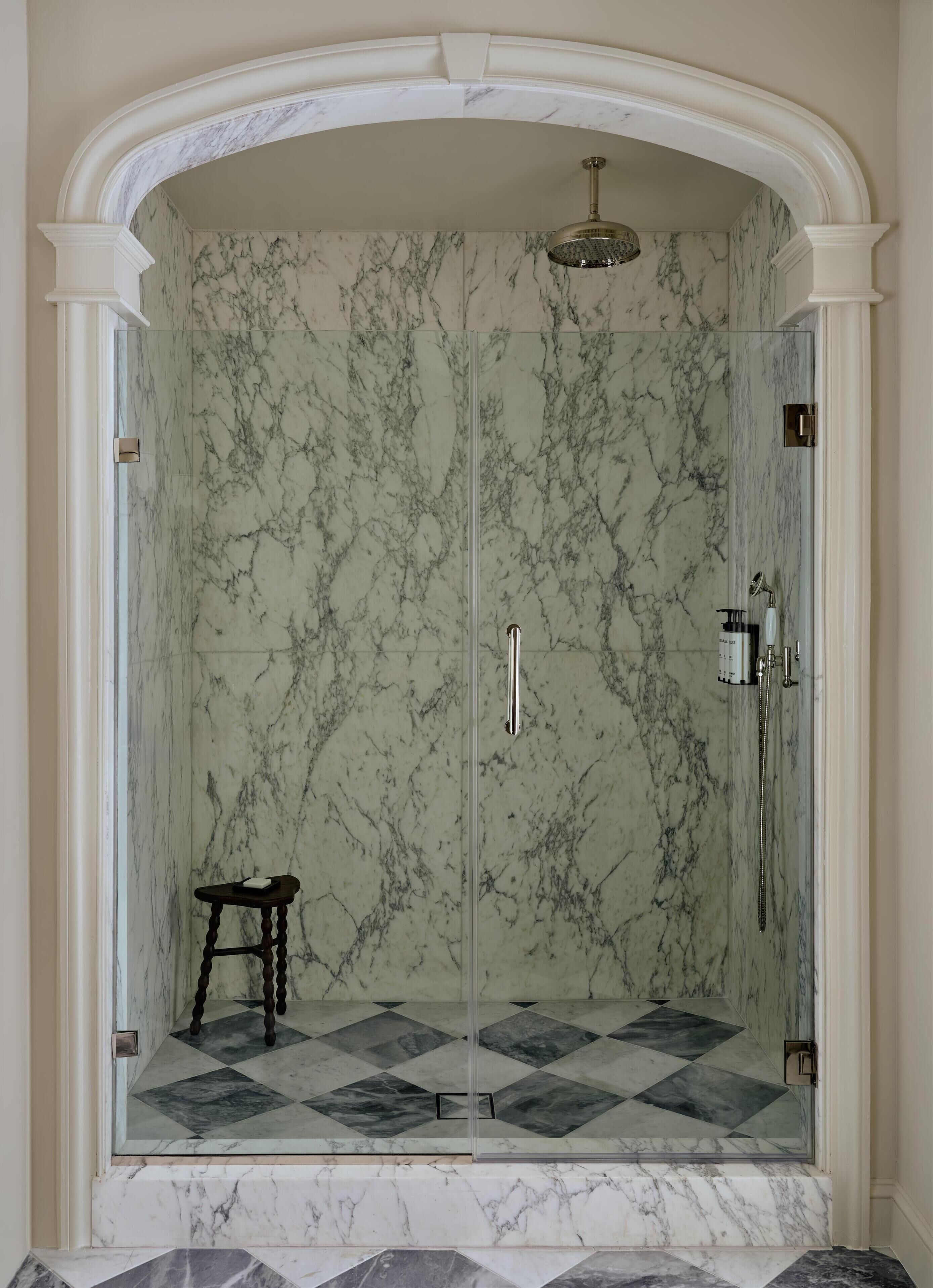 A walk-in shower with a glass door, marble walls, and a geometric tile floor.