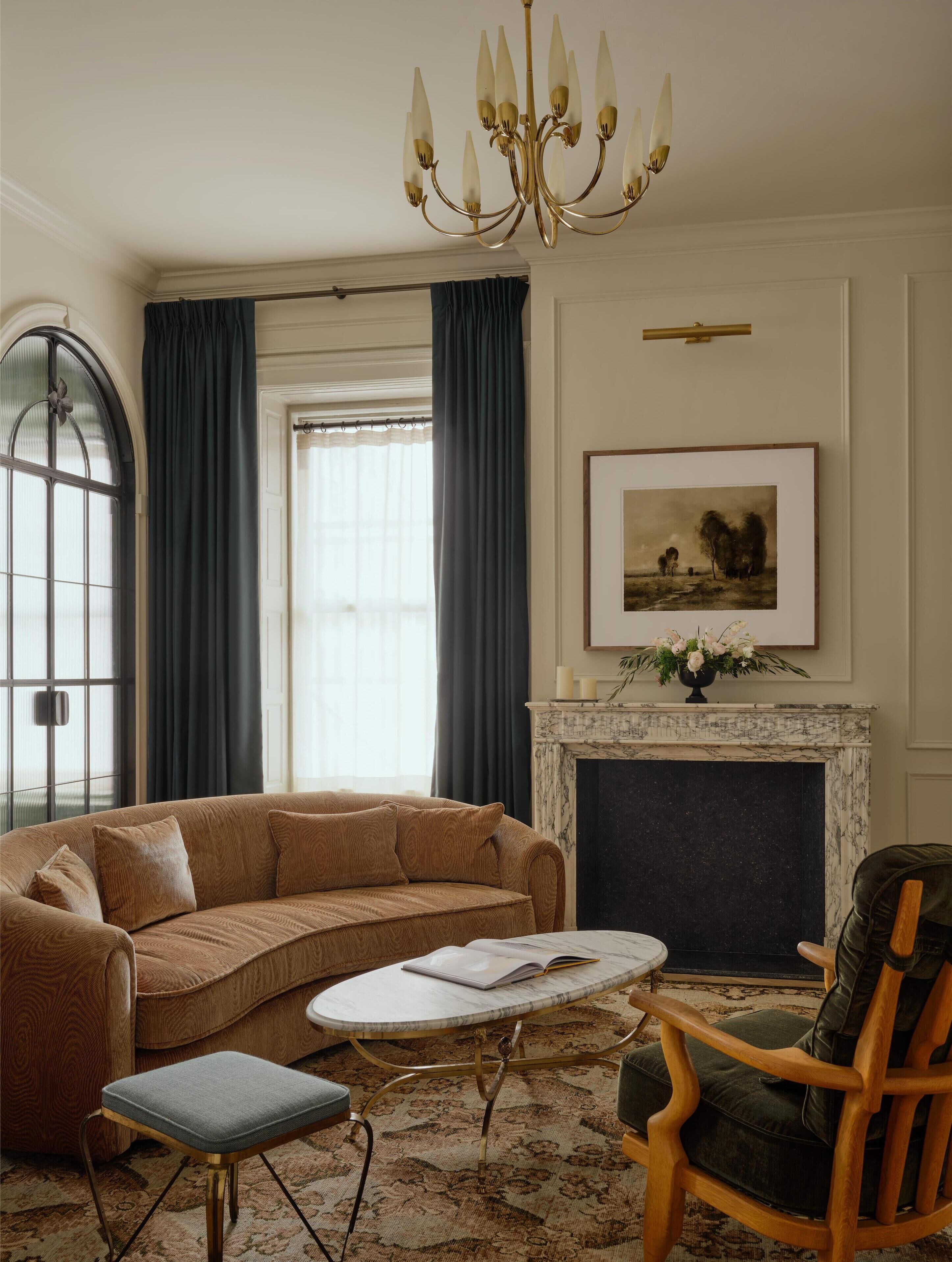 A living room with a brown sofa, a round coffee table, a wooden chair, a fireplace, and a chandelier.