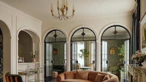 Amplia sala de estar con un sofá grande marrón, una silla de madera y una mesa de centro. Hay tres arcos que dan a otras habitaciones.