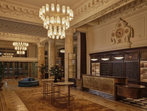 Un lobby imponente con candelabros ornamentales, columnas de mármol, un reloj grande y una exhibición de vinos.