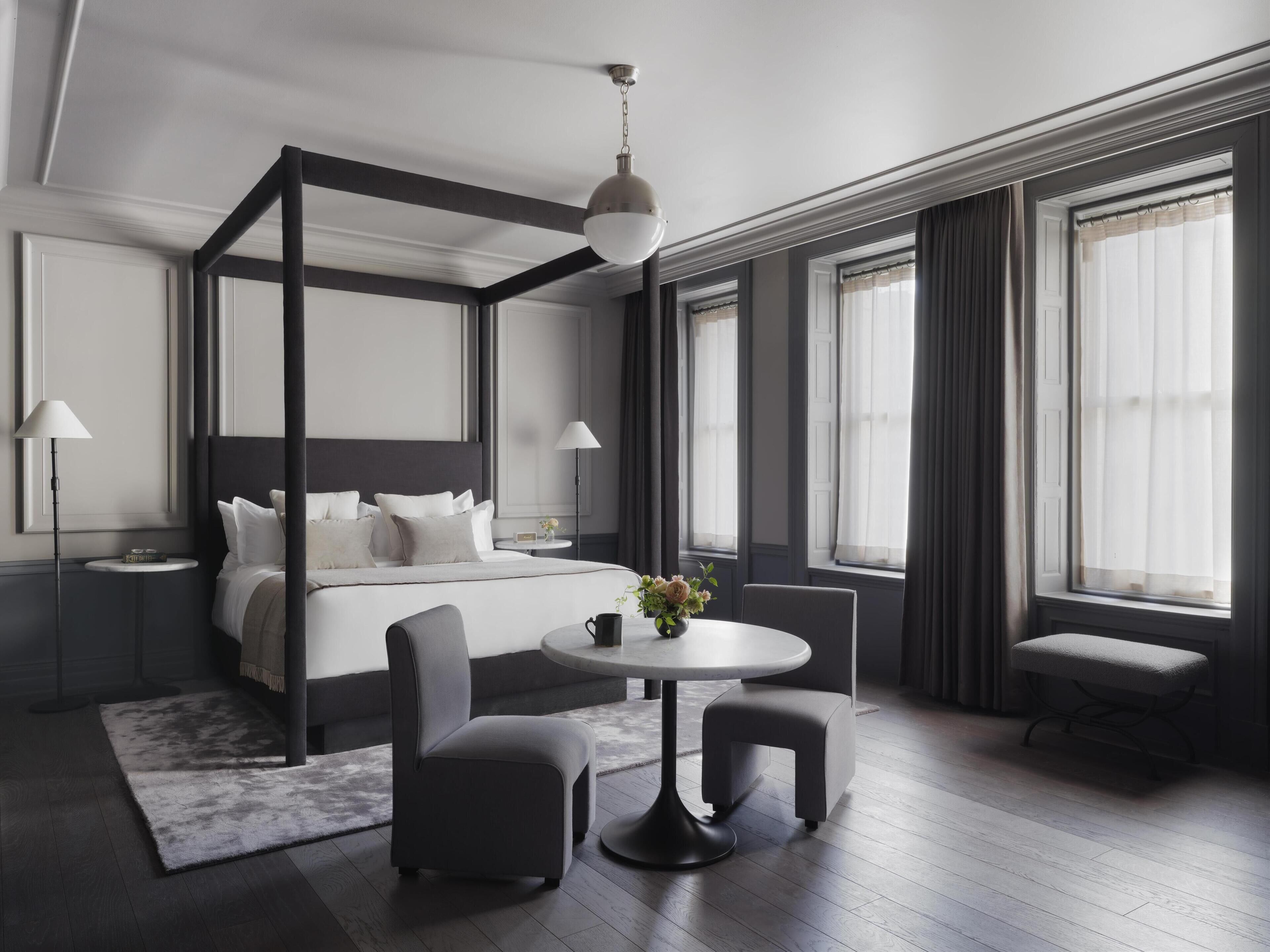 A modern hotel room with a four-poster bed, a round dining table, and a small seating area.