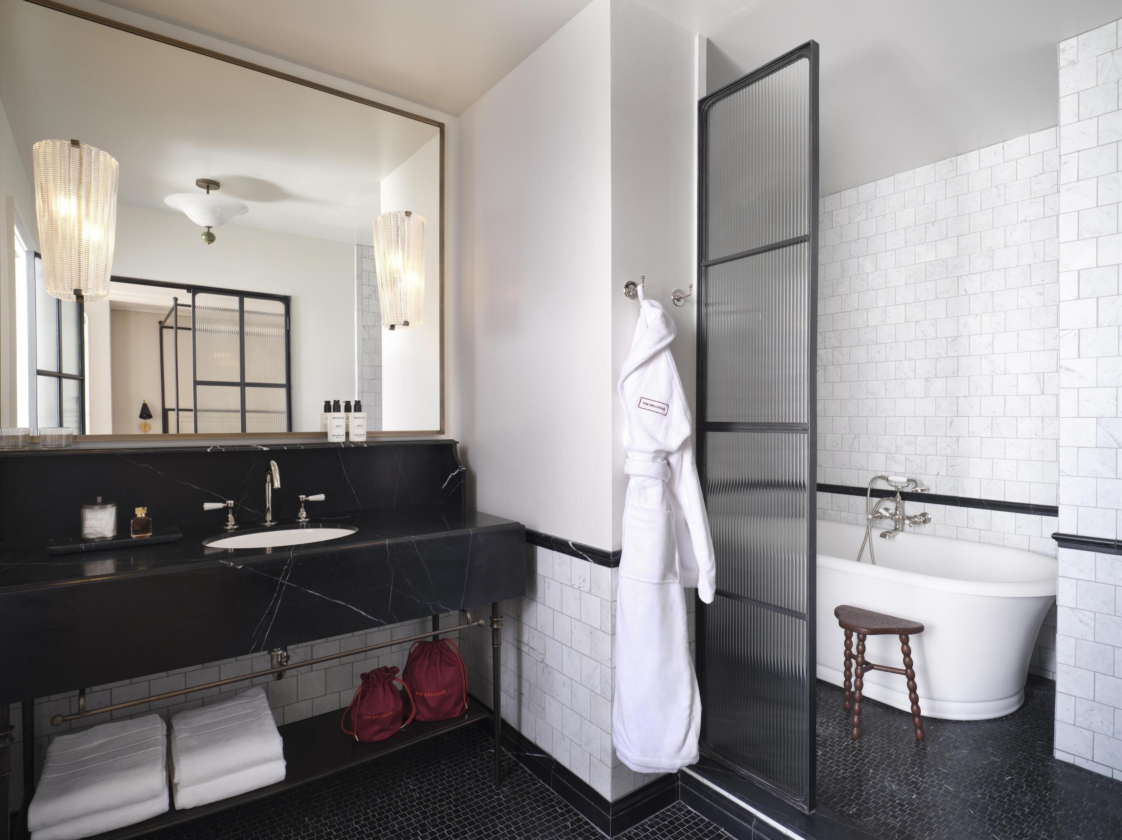 A modern bathroom with a black marble vanity, a large mirror, a white bathtub, and a glass shower enclosure.