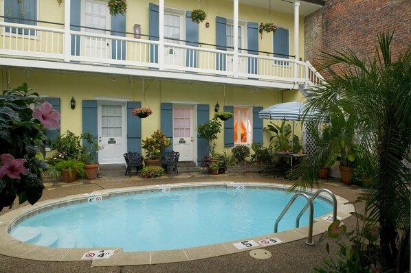 A pool area with a two-story building, outdoor seating, and potted plants. - Hotel St. Pierre®, a French Quarter Inns® Hotel (New Orleans)
