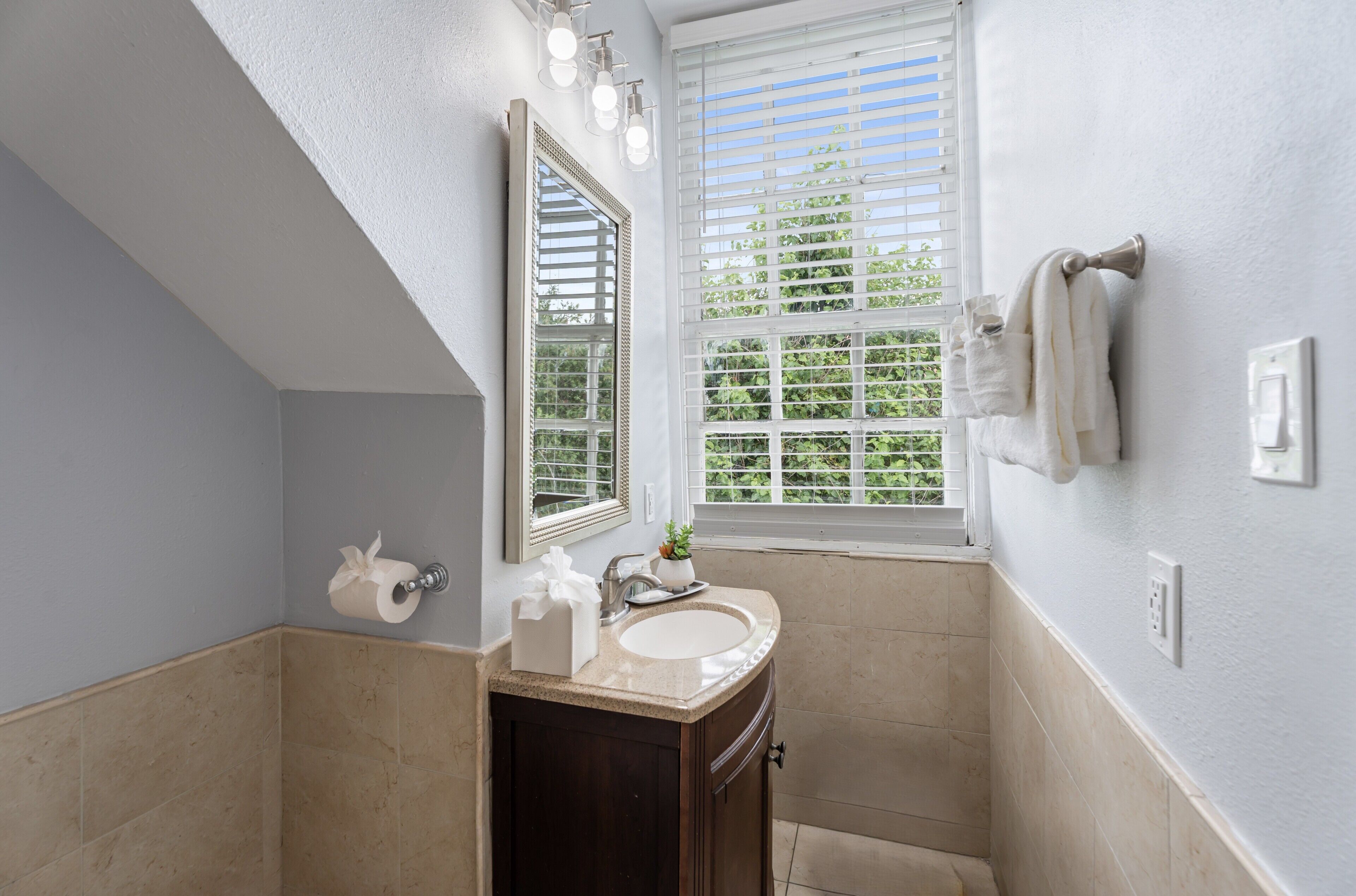 A bathroom with a sink, mirror, towel rack, and window with blinds.