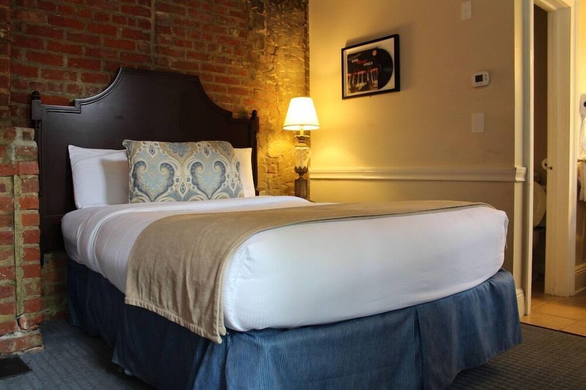 Una cama bien hecha con cabecera, una lámpara de pared y un cuadro en la pared.