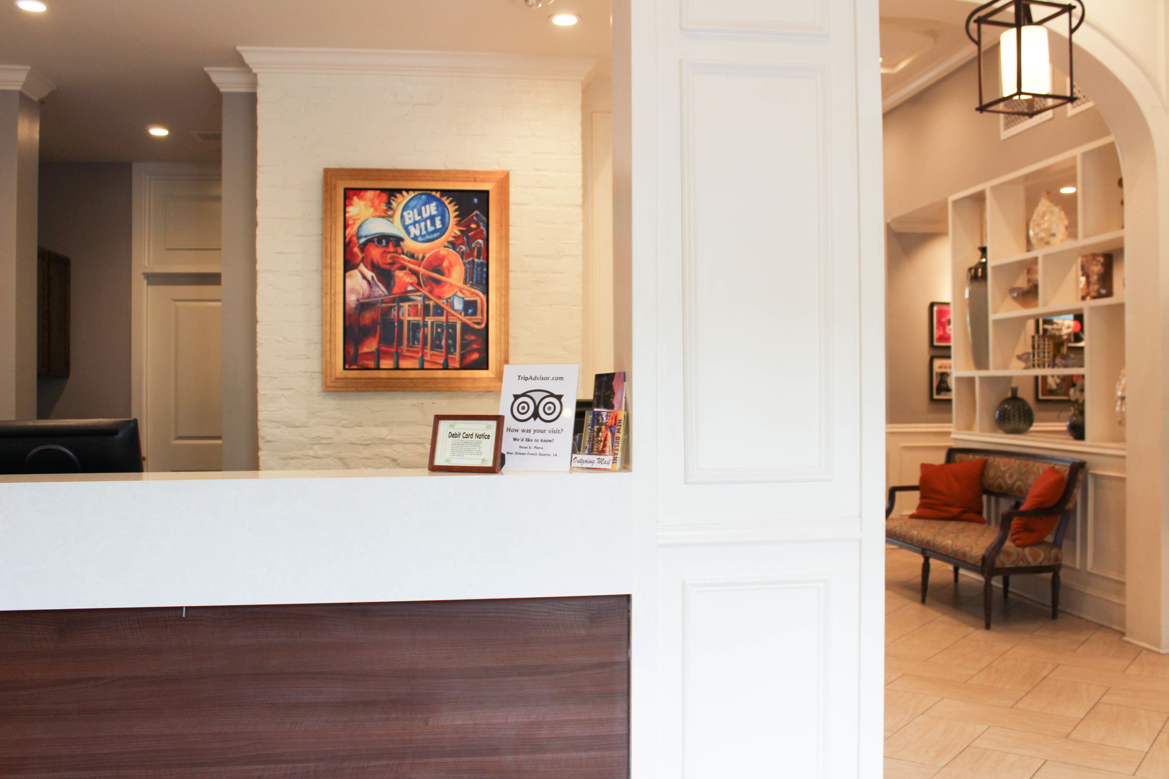 Zona de recepción con pared blanca, una obra de arte enmarcada, un mostrador y una sala de espera con un banco y una silla.
