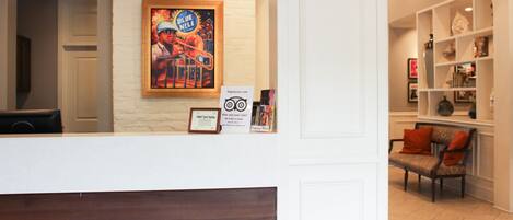Zona de recepción con pared blanca, una obra de arte enmarcada, un mostrador y una sala de espera con un banco y una silla.