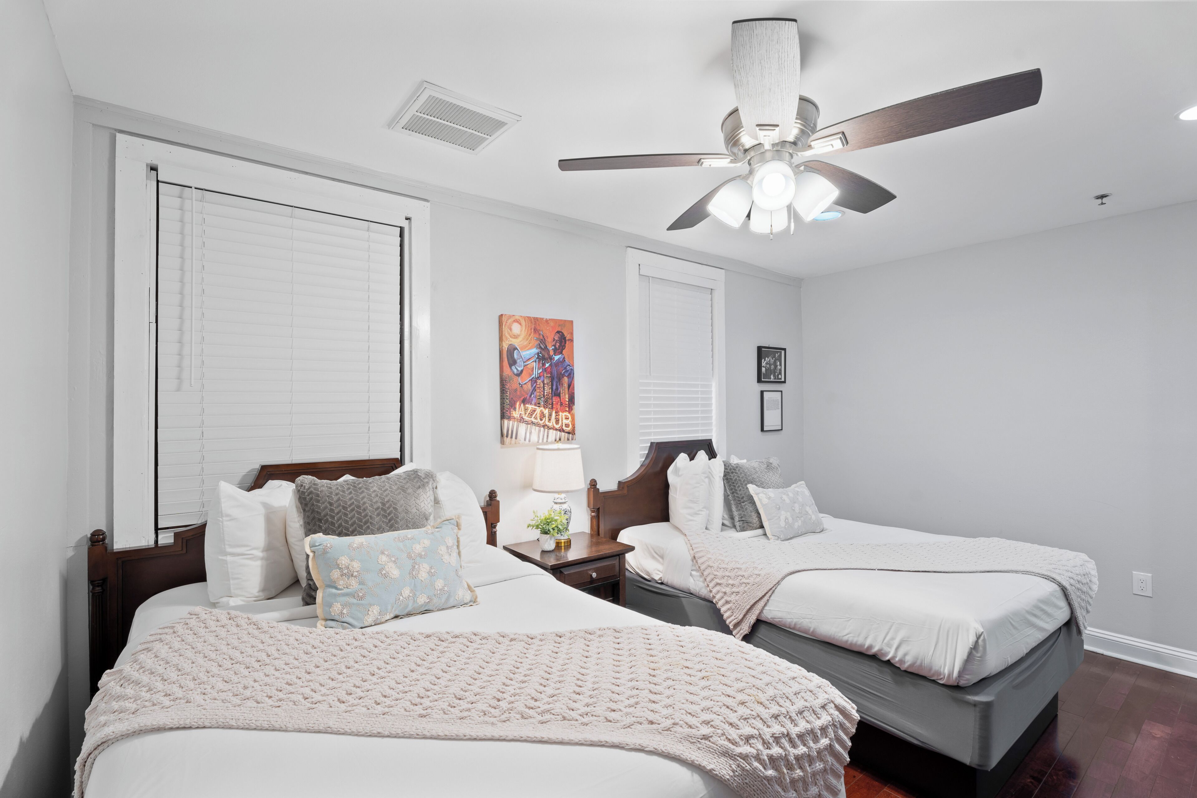 A bedroom with two beds, a ceiling fan, and a painting on the wall.