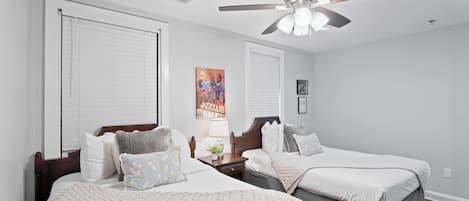 A bedroom with two beds, a ceiling fan, and a painting on the wall.