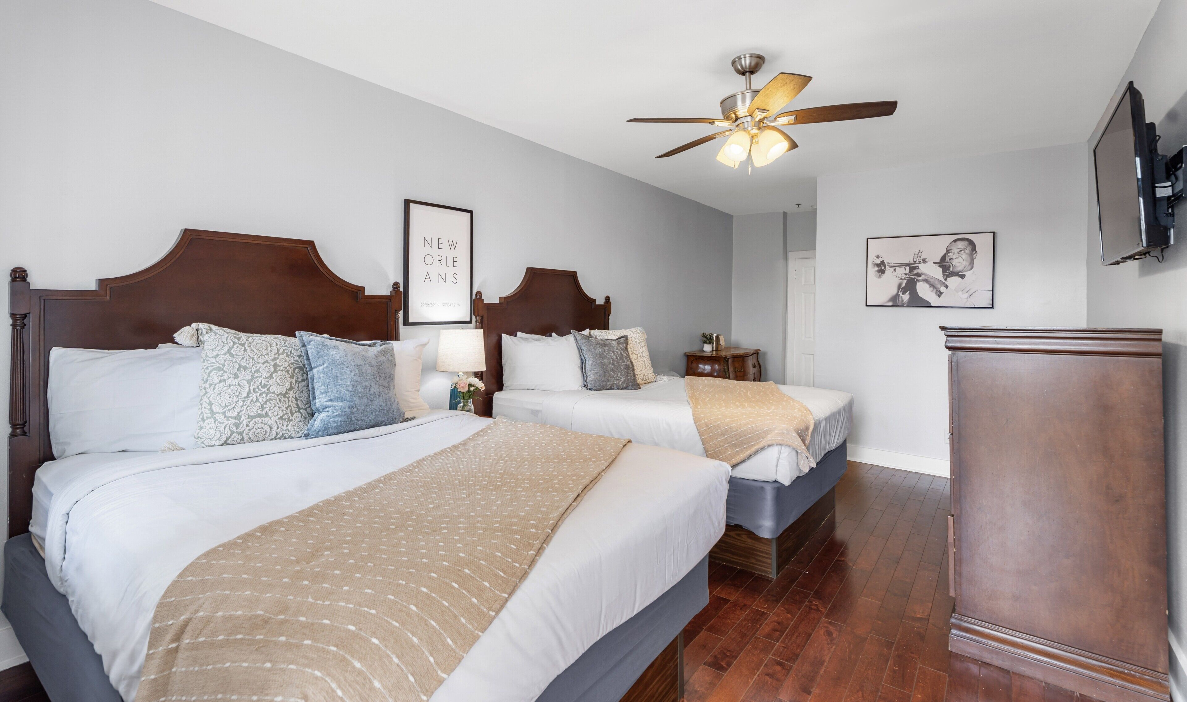 A hotel room with two beds, a ceiling fan, a framed picture on the wall, and a television mounted on the wall.