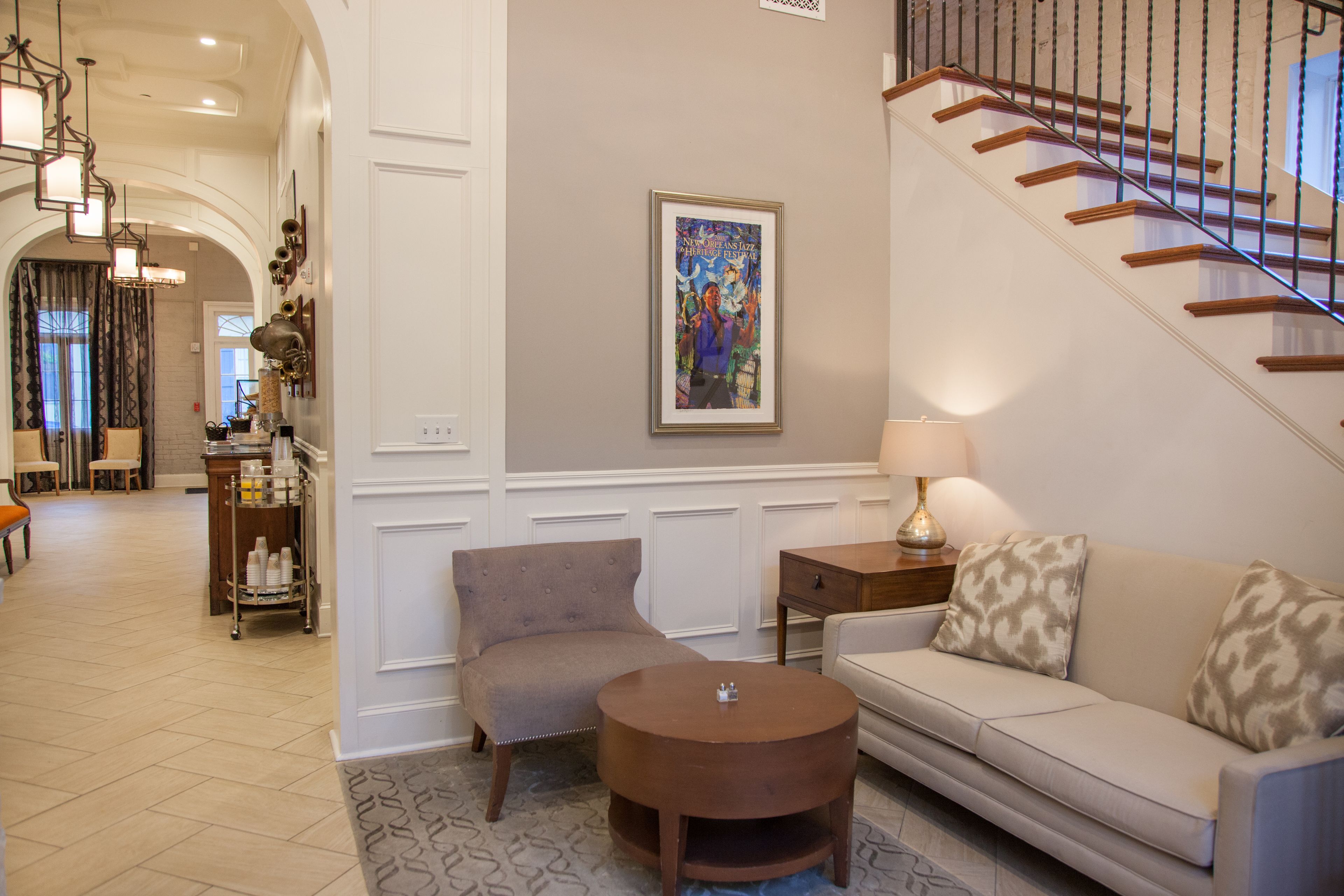Una sala de estar con sofá, sillón y mesa de centro, una escalera y un cuadro en la pared.