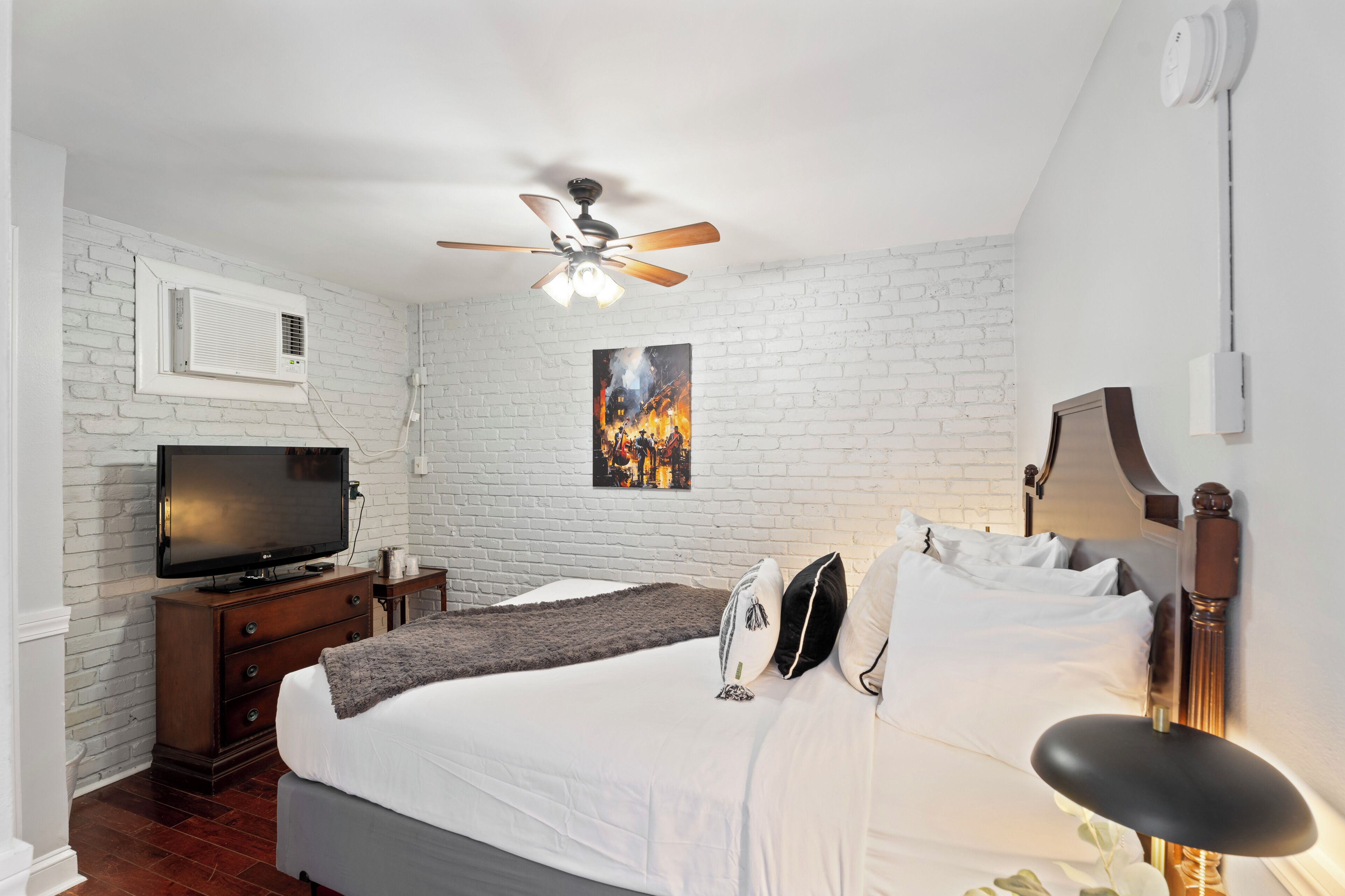 A bedroom with a bed, a ceiling fan, a TV, a painting, and a nightstand.