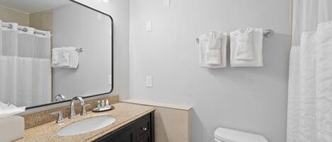 Un bagno con lavandino, specchio, porta asciugamani e water.