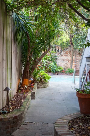 A narrow pathway leading to a pool, surrounded by lush greenery and a brick wall. - Hotel St. Pierre®, a French Quarter Inns® Hotel (New Orleans)