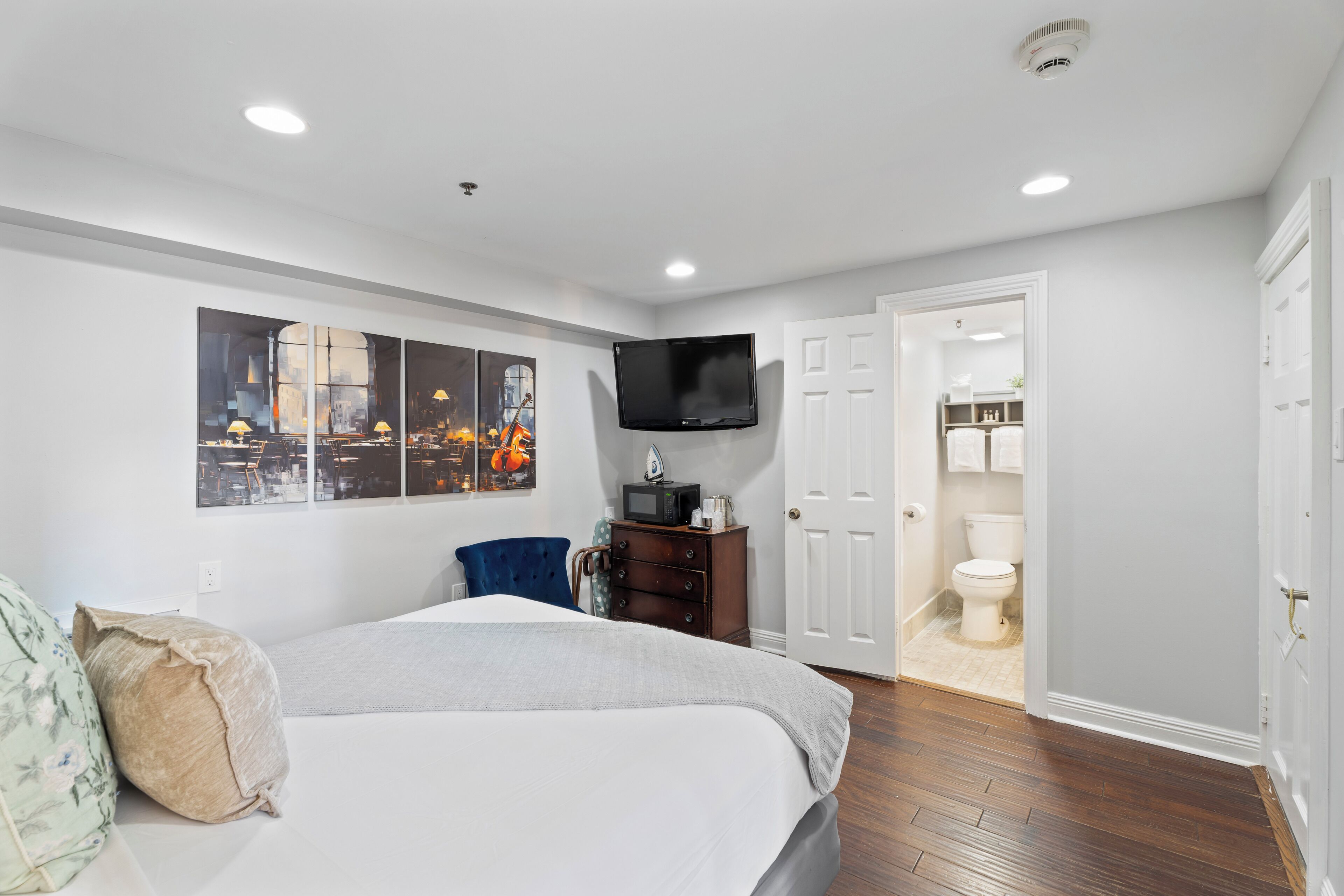 A bedroom with a bed, a TV, a dresser, and a door leading to a bathroom.