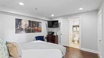 A bedroom with a bed, a TV, a dresser, and a door leading to a bathroom.
