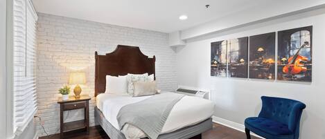 Une chambre à coucher avec un lit, une table de chevet, une chaise, un mur en briques et des œuvres d’art accrochées au mur.