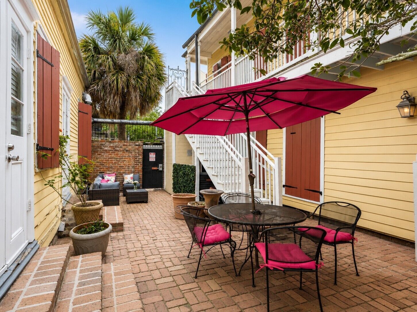 A patio with a round table and chairs, a red umbrella, and a staircase leading to an upper level.