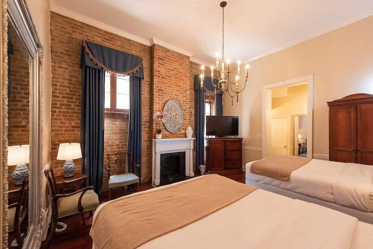 A hotel room with two beds, a fireplace, a television, and a chandelier.