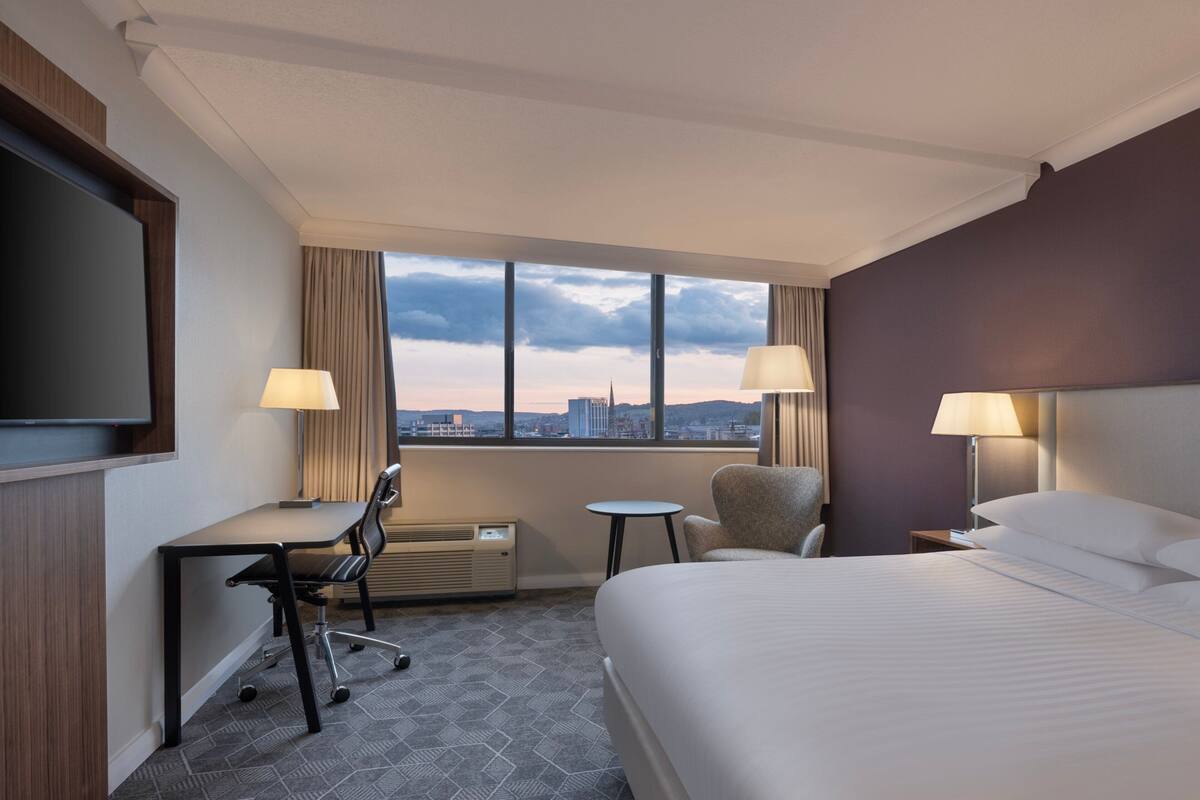 Ein Hotelzimmer mit Bett, Schreibtisch, Stuhl und Fernseher.