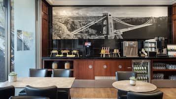 Een moderne hotellobby met een groot muurschildering van een brug, een bar met koffieautomaten en zitgedeeltes.