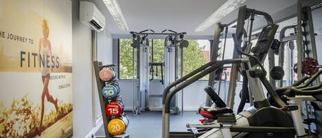 Un gimnasio con equipo de ejercicio, un cartel en la pared y una ventana con vista a árboles.