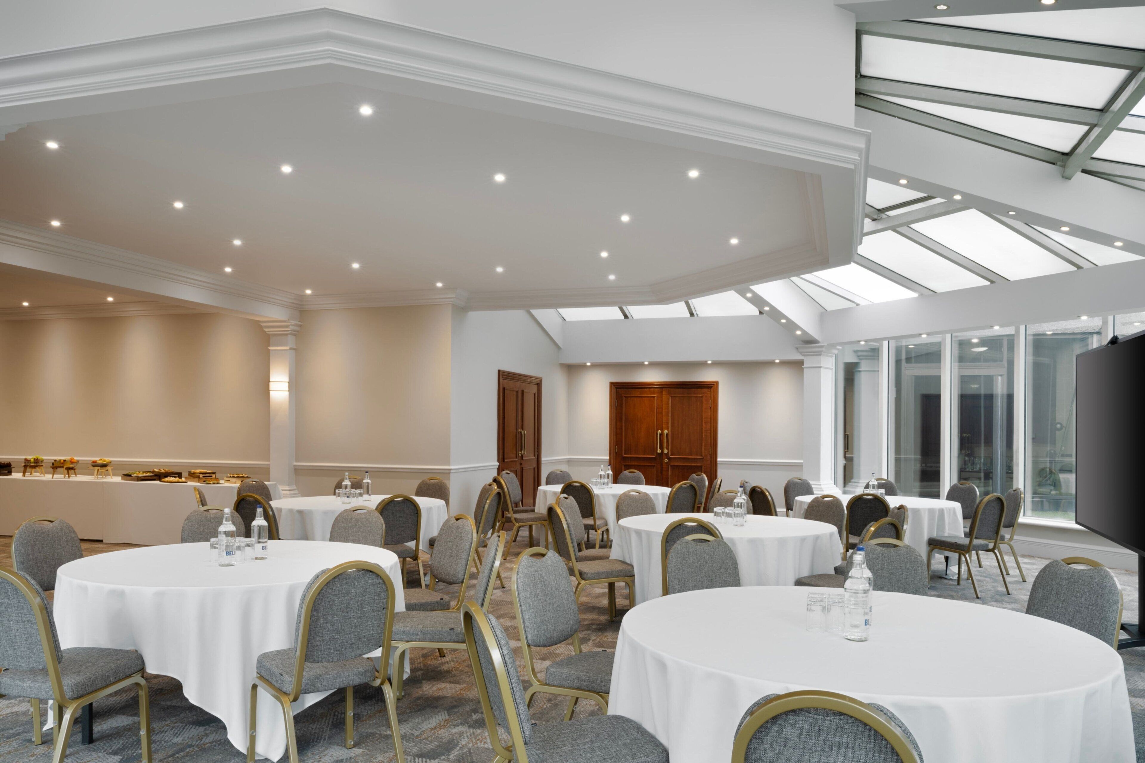 A conference room with round tables, grey upholstered chairs, and a high ceiling with skylights.
