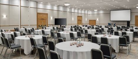 Une salle de conférence dotée de plusieurs tables rondes, chacune étant agrémentée de chaises et de verres à eau.