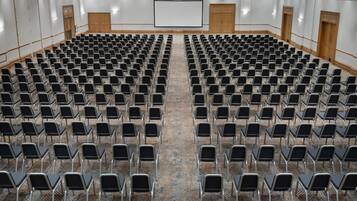 A large conference room with rows of chairs, a projector screen, and wooden doors.
