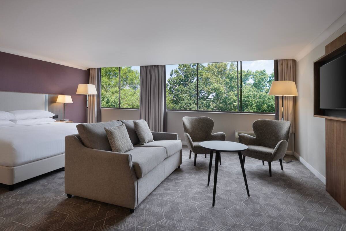 Ein Hotelzimmer mit einem Bett, einer Couch, zwei Sesseln, einem kleinen Tisch und einem Fernseher.