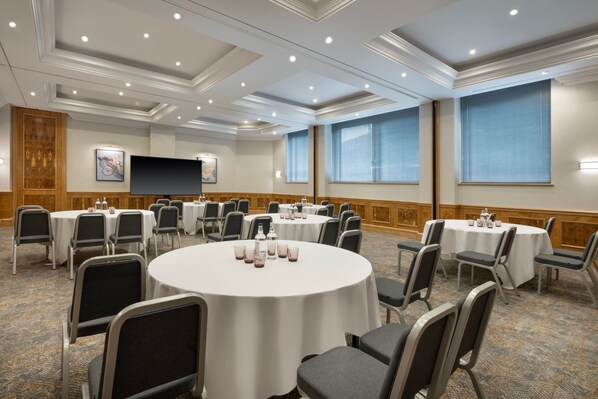 Un salón de conferencias con mesas redondas, sillas y una pantalla grande.