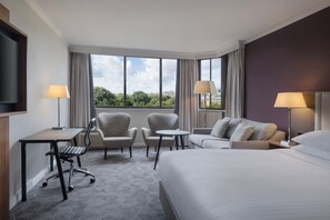 Relax in a spacious room with a large bed, seating area, and desk, offering a city view.