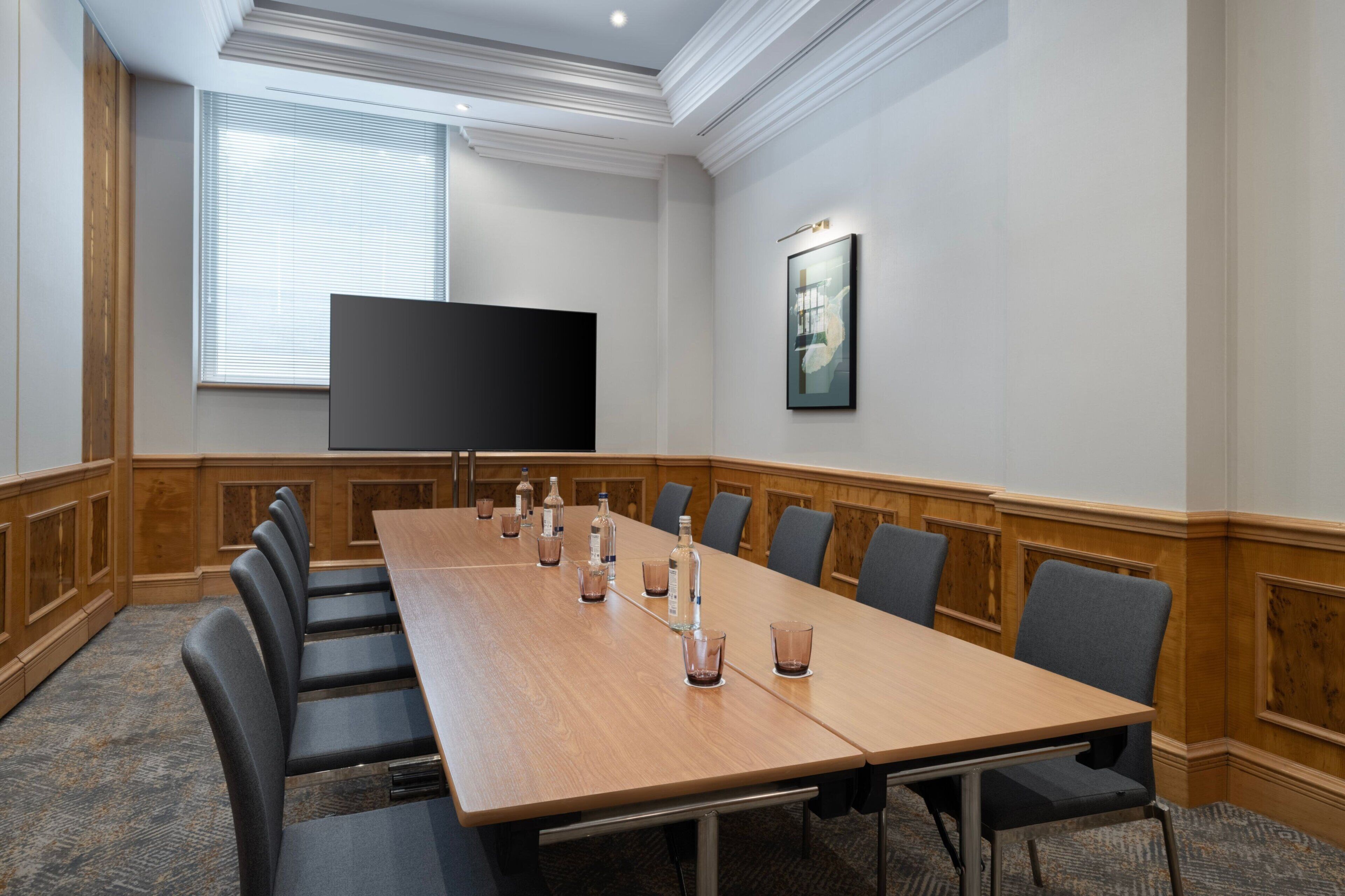 A conference room with a long table, chairs, a flat-screen TV, and a framed picture on the wall.
