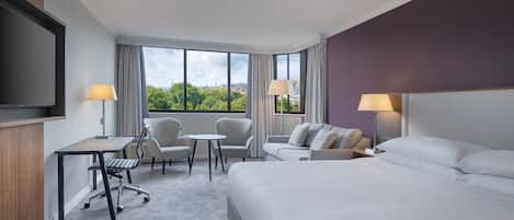 A hotel room with a bed, a desk, two chairs, a sofa, and a TV.