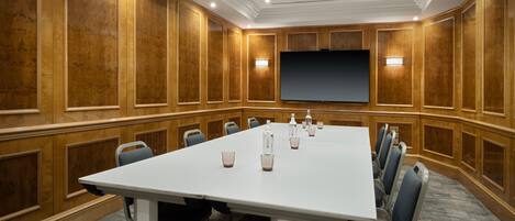 A conference room with a long table, chairs, a projector screen, and wooden paneling.