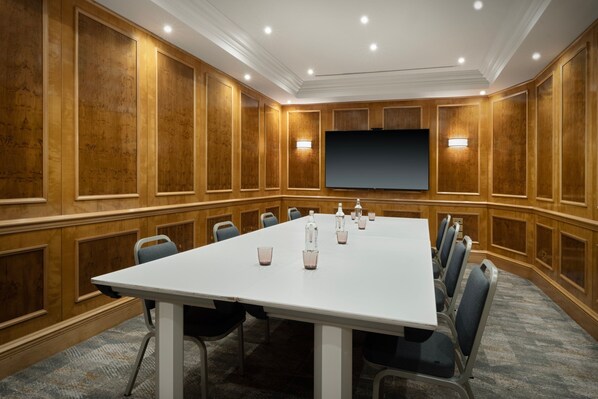 Un salón de conferencias con una larga mesa, sillas, una pantalla de proyector y paneles de madera.