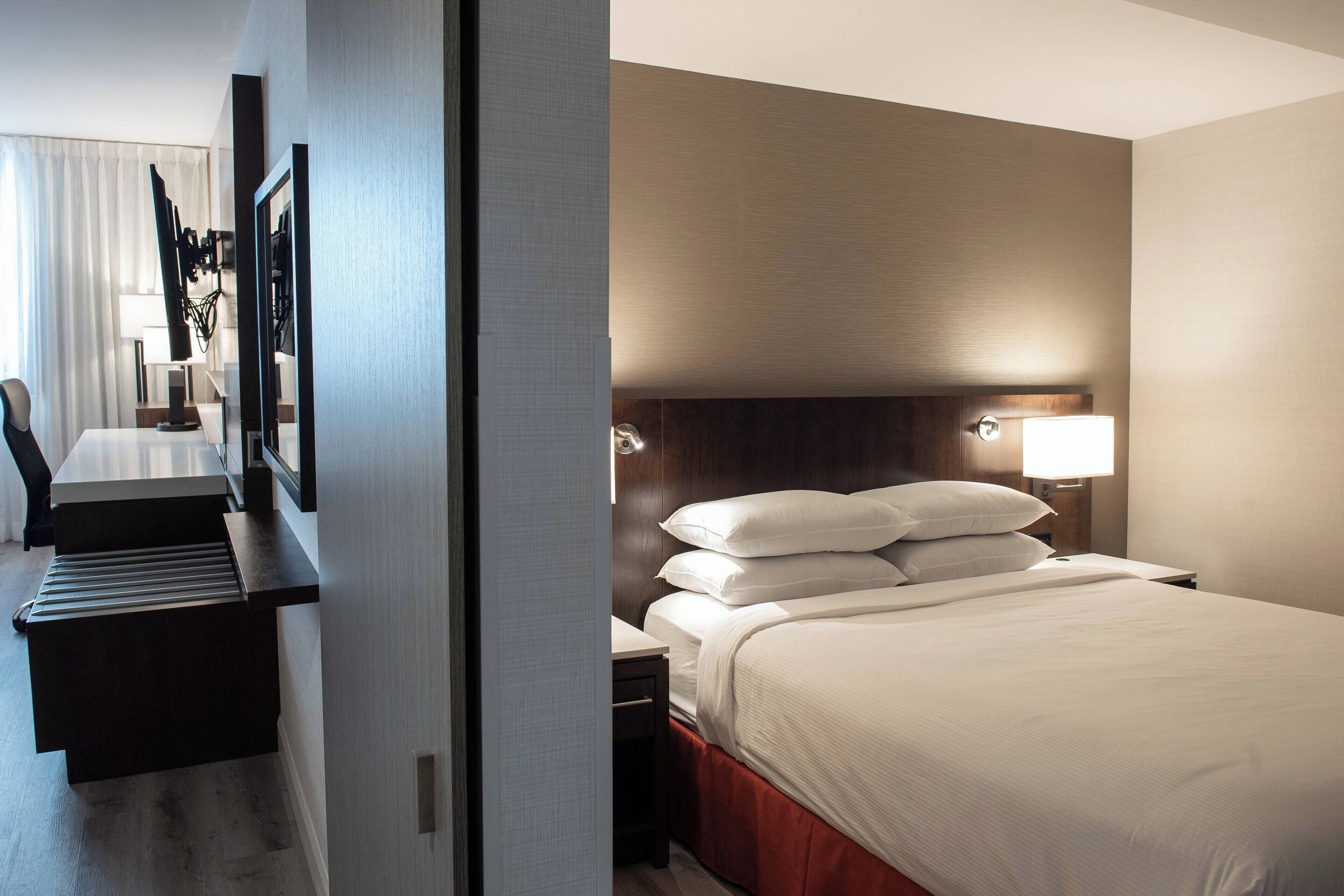 Une chambre d’hôtel comprenant un lit, une table de chevet, une lampe et un bureau avec une chaise.