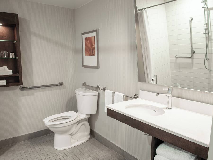 Ein modernes Badezimmer mit Toilette, Waschbecken und Dusche. Es gibt Regale mit Pflegeprodukten und ein gerahmtes Bild an der Wand.