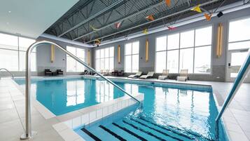 An indoor swimming pool with clear water, a metal ladder, and sunlit windows.