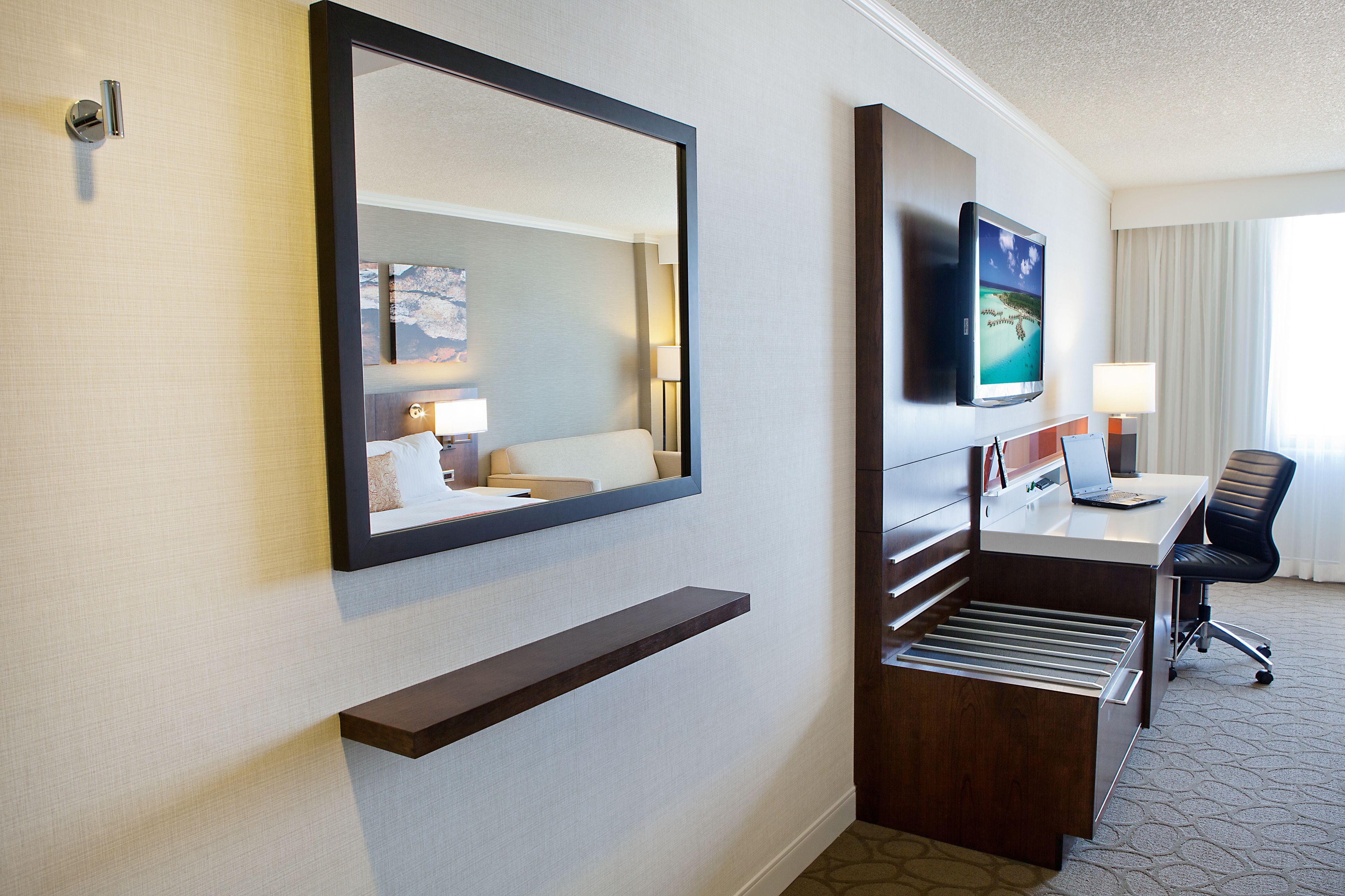 Hotelkamer met een grote spiegel, een bureau met een computer, een stoel en een aan de muur bevestigde televisie.