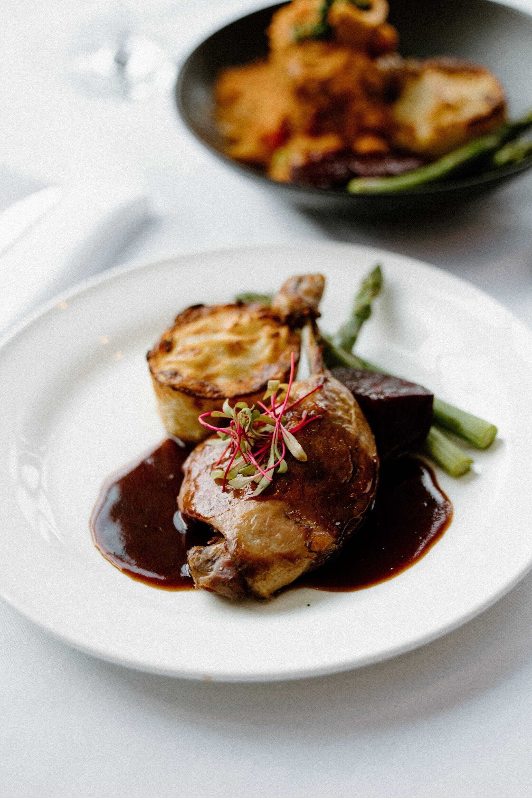 A plate of food with a duck leg, asparagus, and a beet.