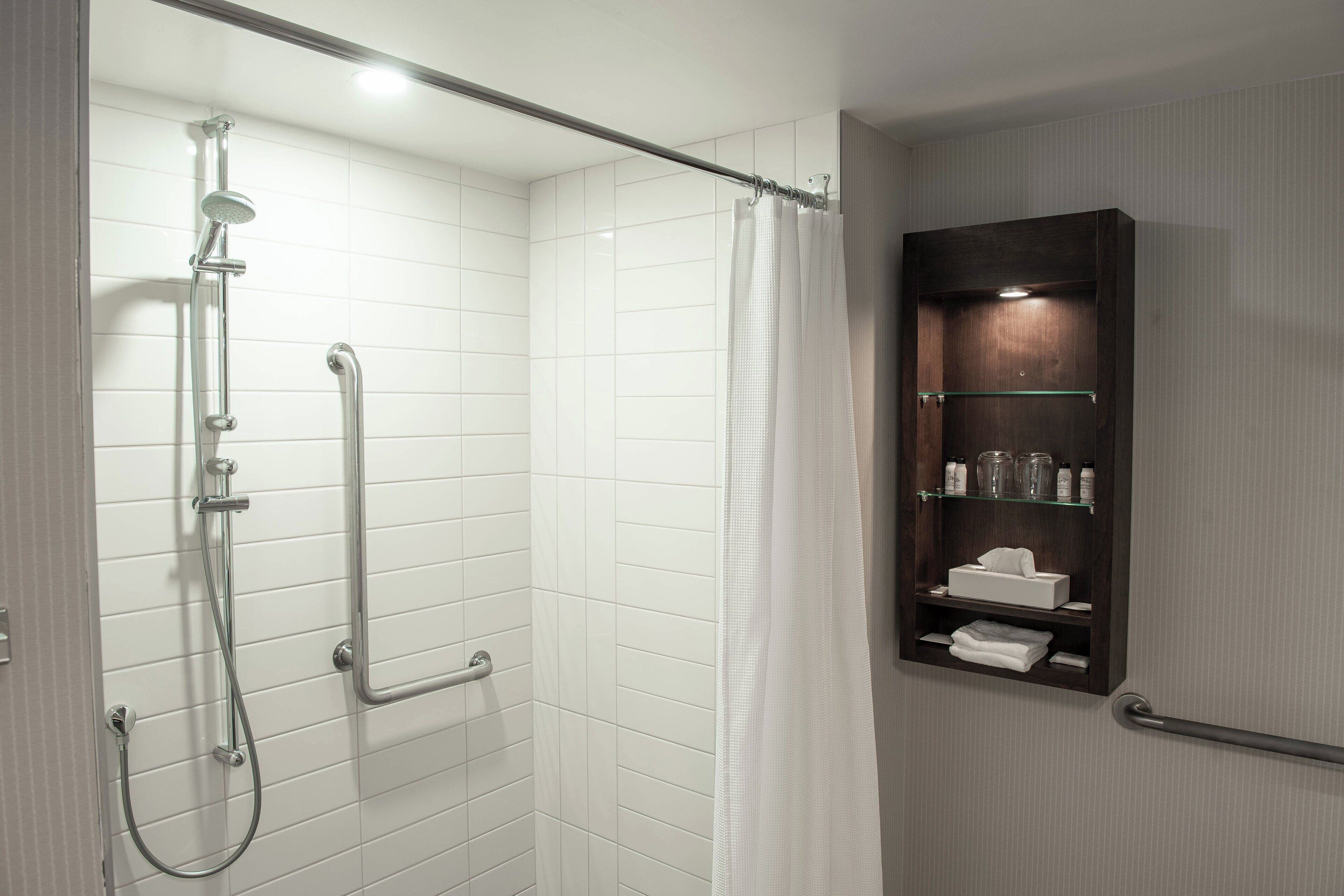 A shower with a glass enclosure, a handrail, and a towel rack.
