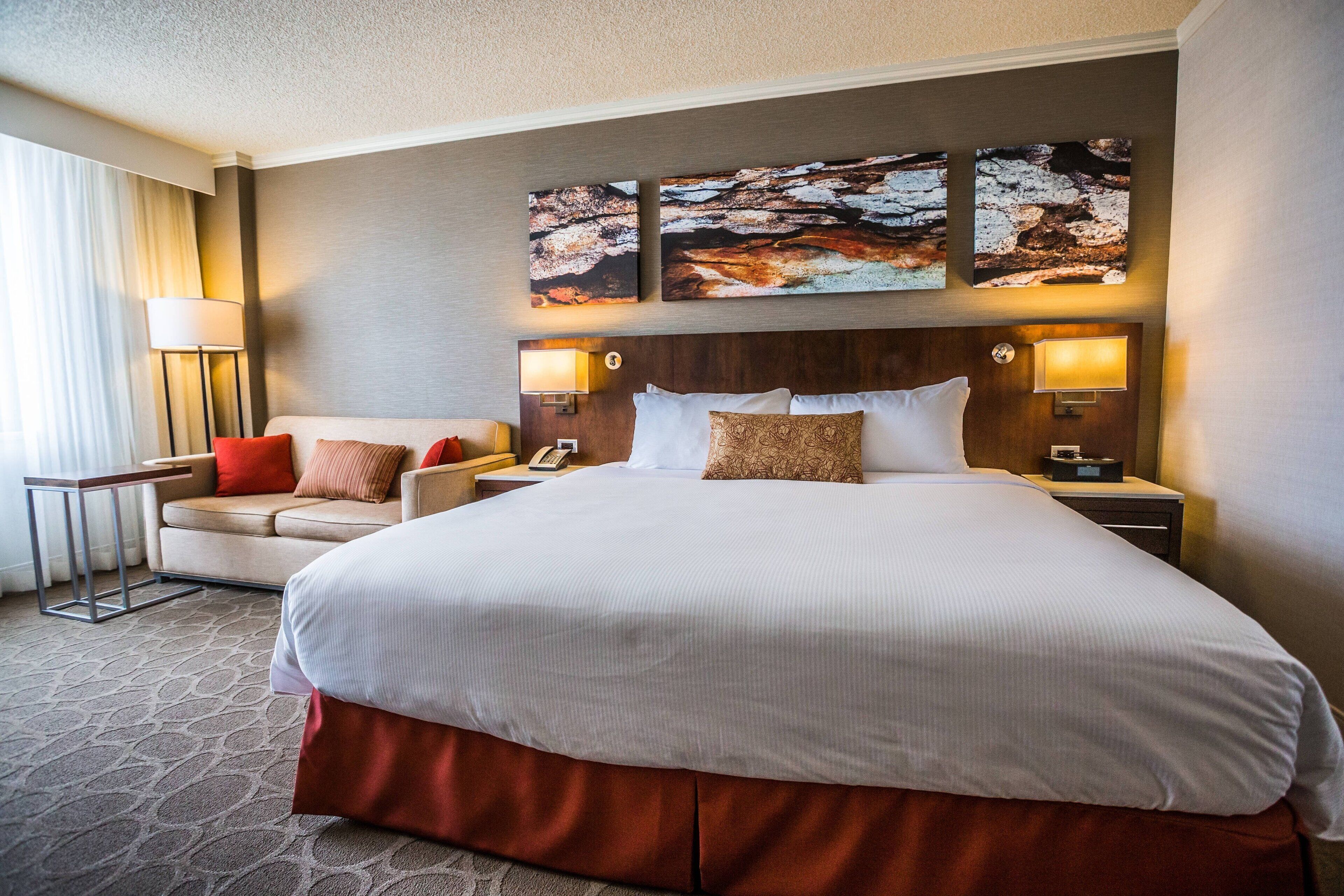 A hotel room with a large bed, two bedside tables, a nightstand, a sofa, and a lamp.