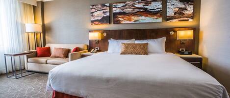 A hotel room with a large bed, two bedside tables, a nightstand, a sofa, and a lamp.