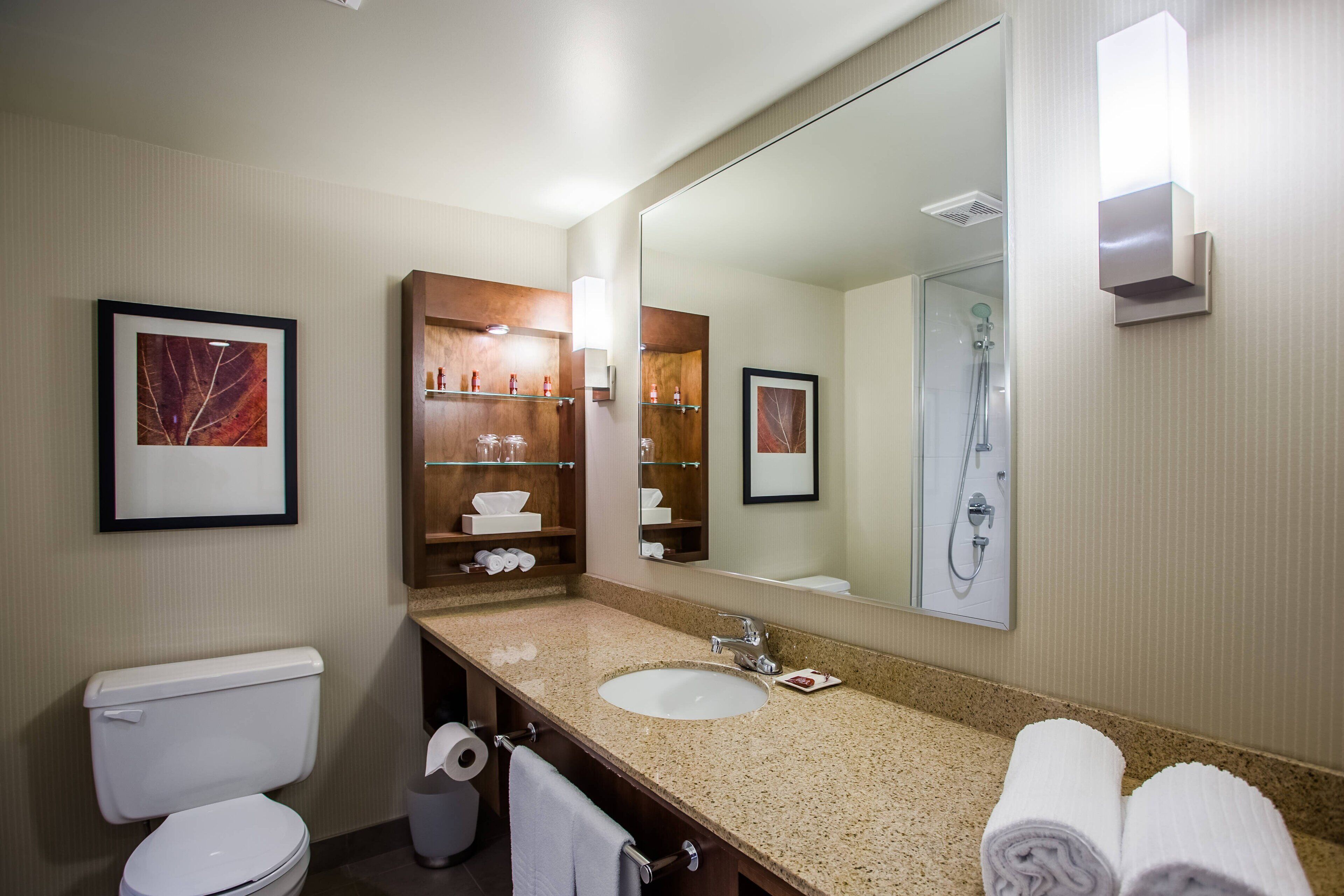 A bathroom with a toilet, sink, and shower. There are framed pictures on the wall and a towel rack with towels.