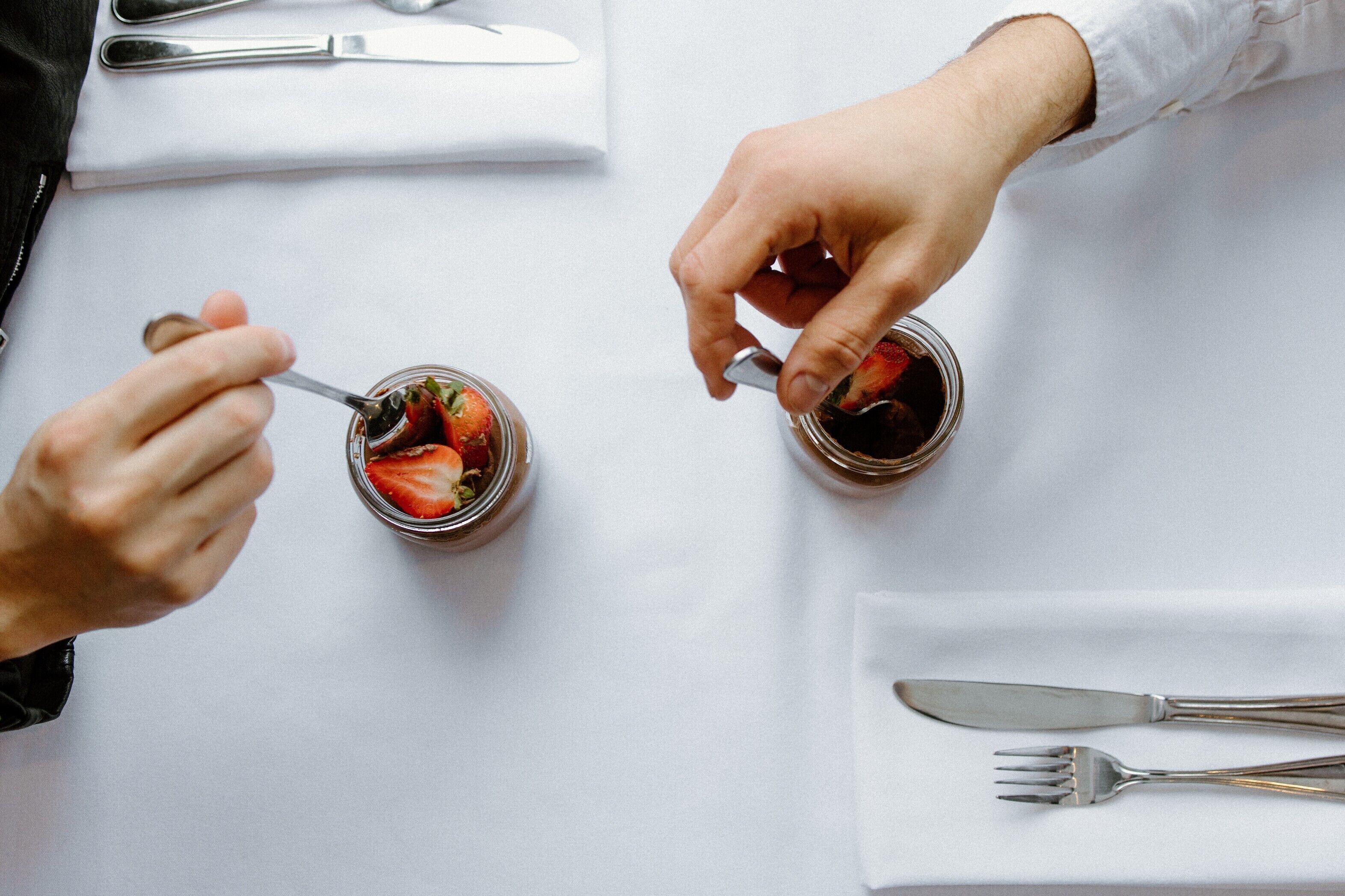 Una mesa de comedor con una persona comiendo de un frasco, un tenedor y un cuchillo sobre un mantel blanco.